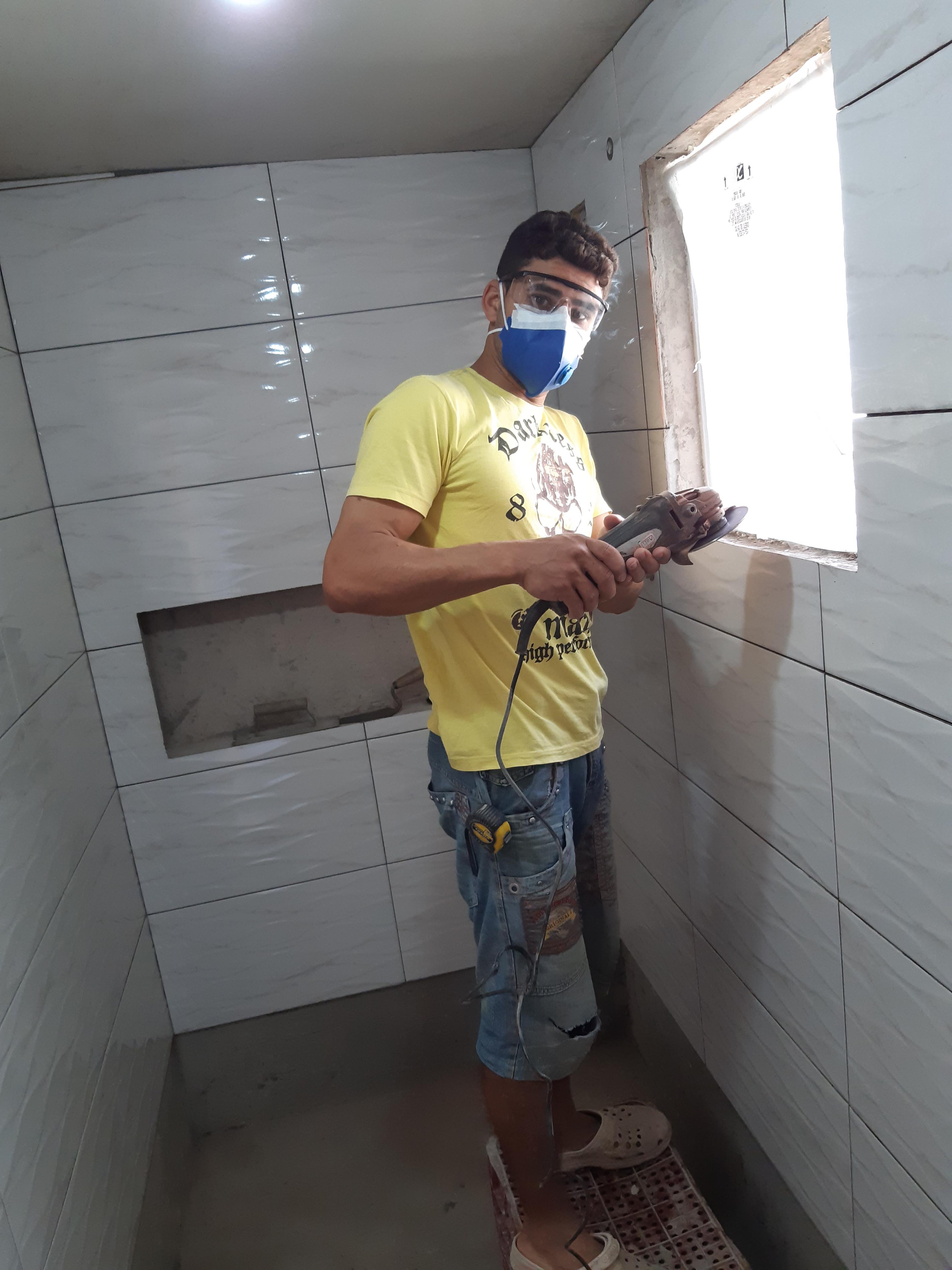 um homem usando máscara e óculos de proteção trabalhando em uma construção com ferramenta elétrica em uma área com azulejos