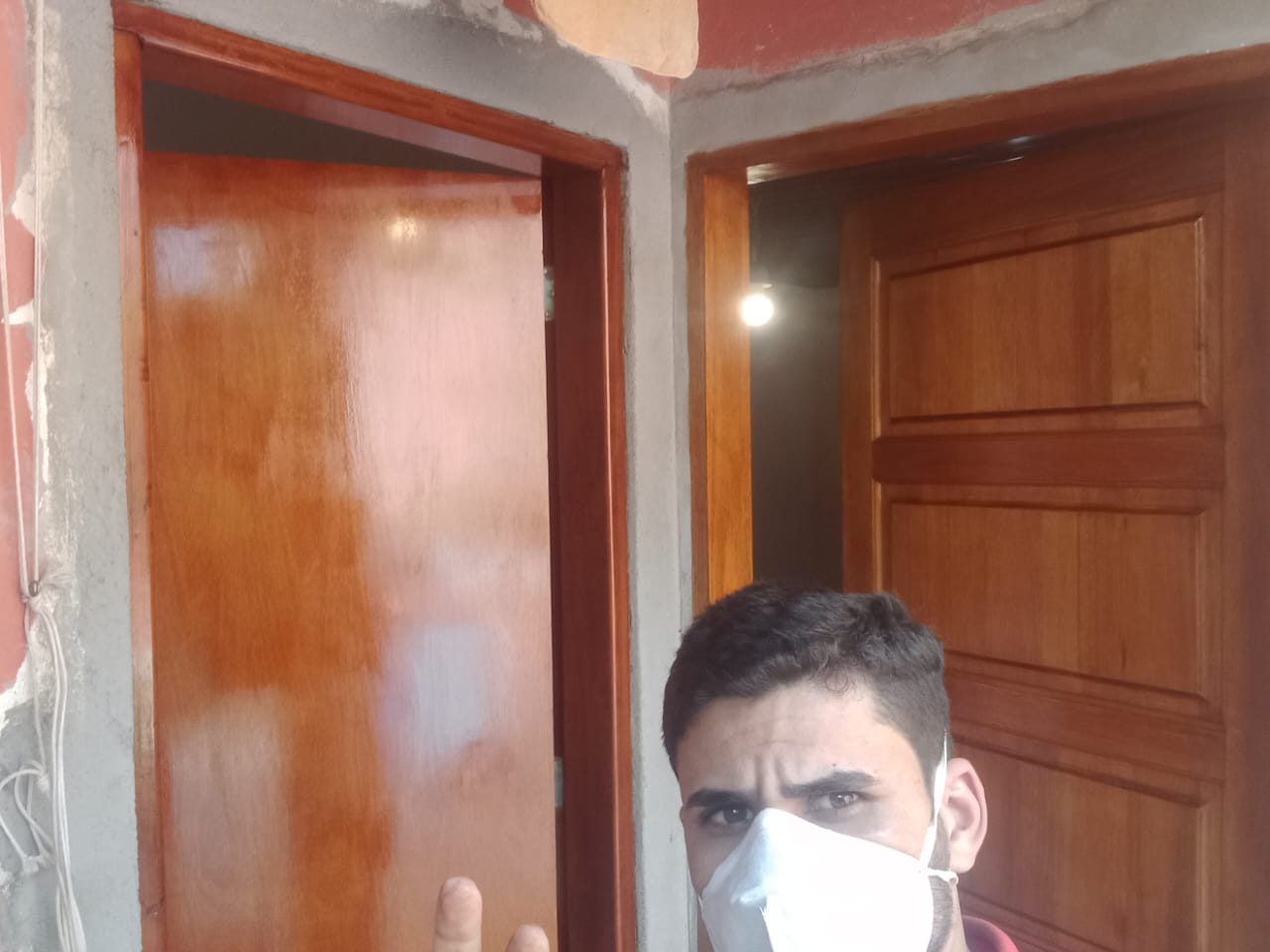 homem de máscara branca em frente a duas portas de madeira em ambiente com parede em acabamento