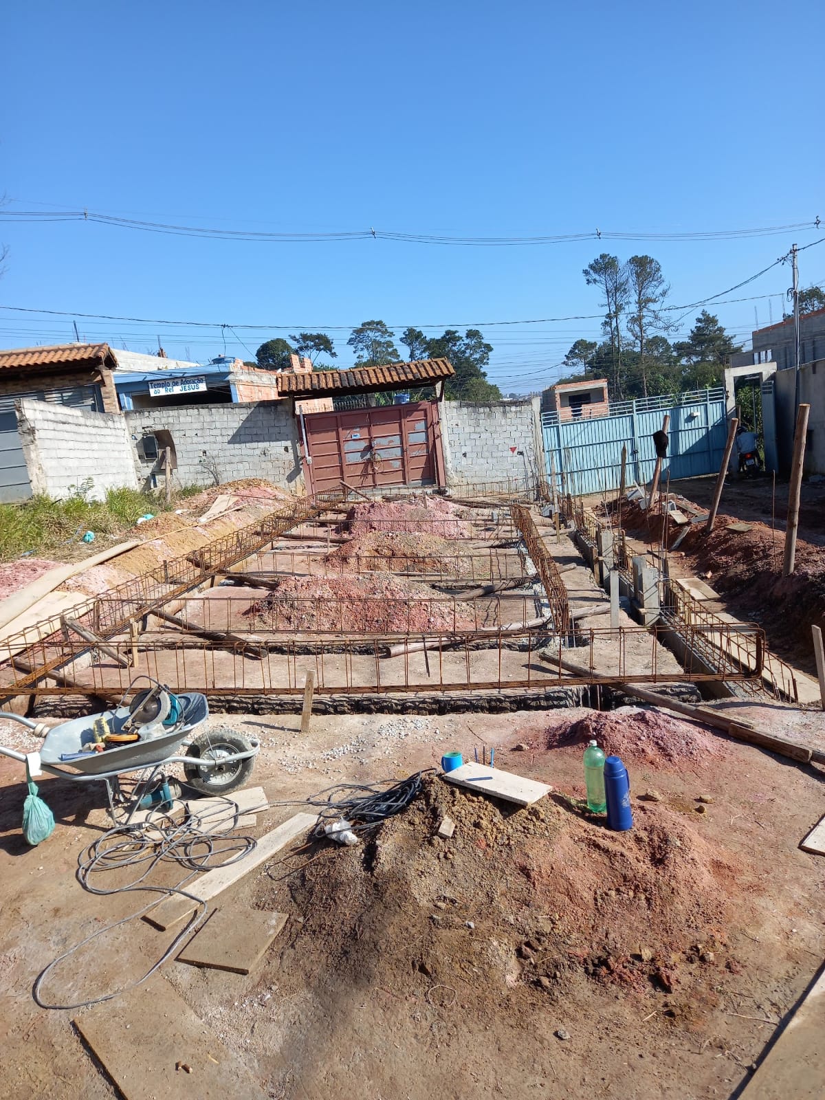 Canteiro externo com armação de ferro da fundação, terra vermelha e ferramentas sob céu azul