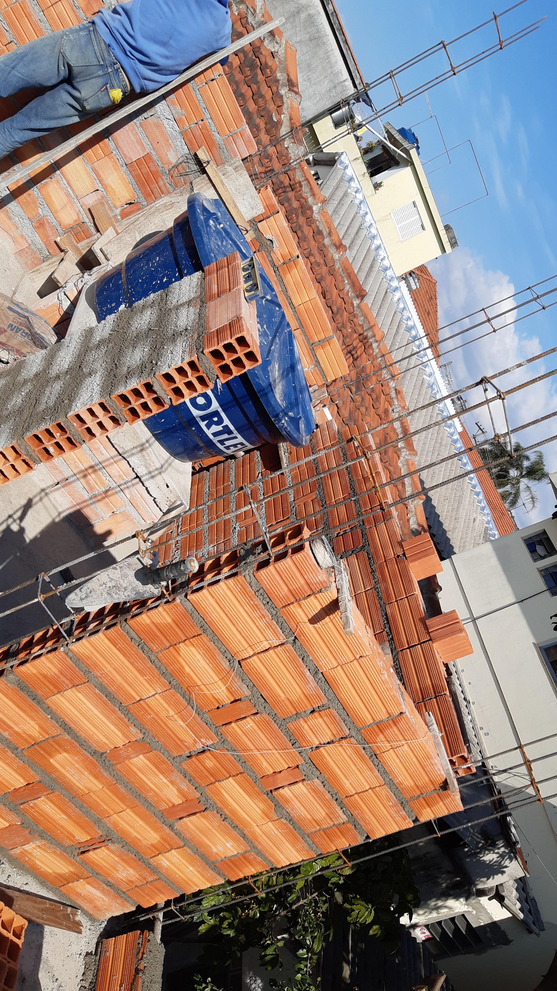 Alvenaria em tijolo vermelho com balde de massa e ferragens